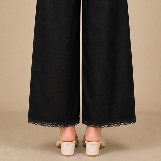 Black wide-leg trousers with a delicate black lace hem, shown from the back on a model wearing off-white block-heeled mule sandals against a solid beige background.
