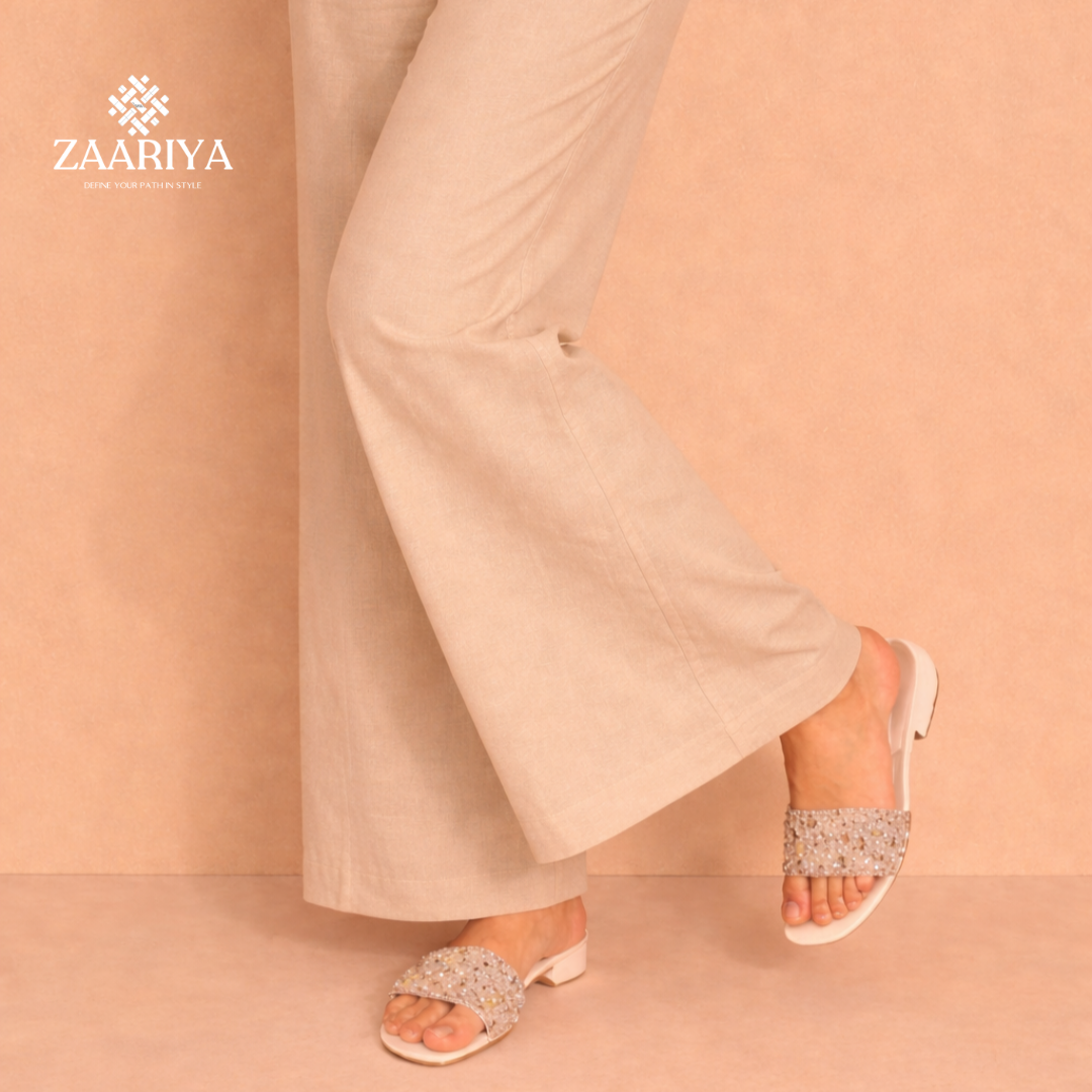 Woman wearing beige pants and embellished sandals on a peach background with Zaariya branding.