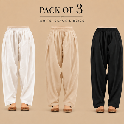 Three pairs of loose, high-waisted pleated shalwars shown from the back on a beige studio background, labeled 'PACK OF 3' with color options 'WHITE, BLACK & BEIGE'. The pants are shown in white, beige, and black, paired with tan flat shoes.